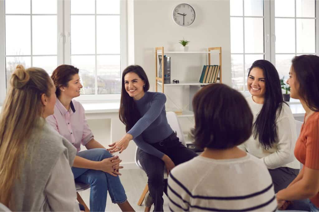 A group therapy session with a supportive and diverse group of individuals seated in a circle, sharing and smiling in a bright, welcoming space. This image represents Key Healthcare’s commitment to providing group therapy for adolescents, focusing on shared experiences, emotional growth, and peer support as part of their evidence-based mental health and recovery programs.