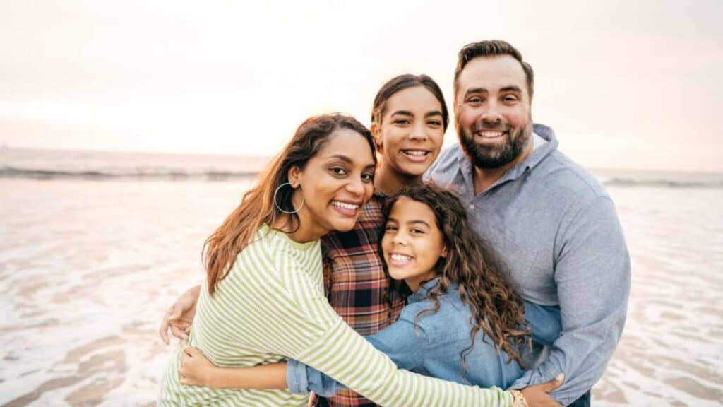 Smiling family hugging on the beach, showing strong emotional bonds and support for their teen’s well-being.