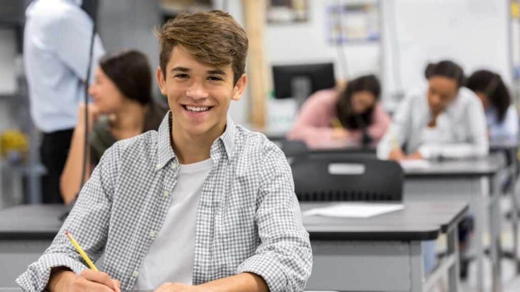 Teen boy smiling in classroom, participating in academic learning, key educational component of residential treatment programs.